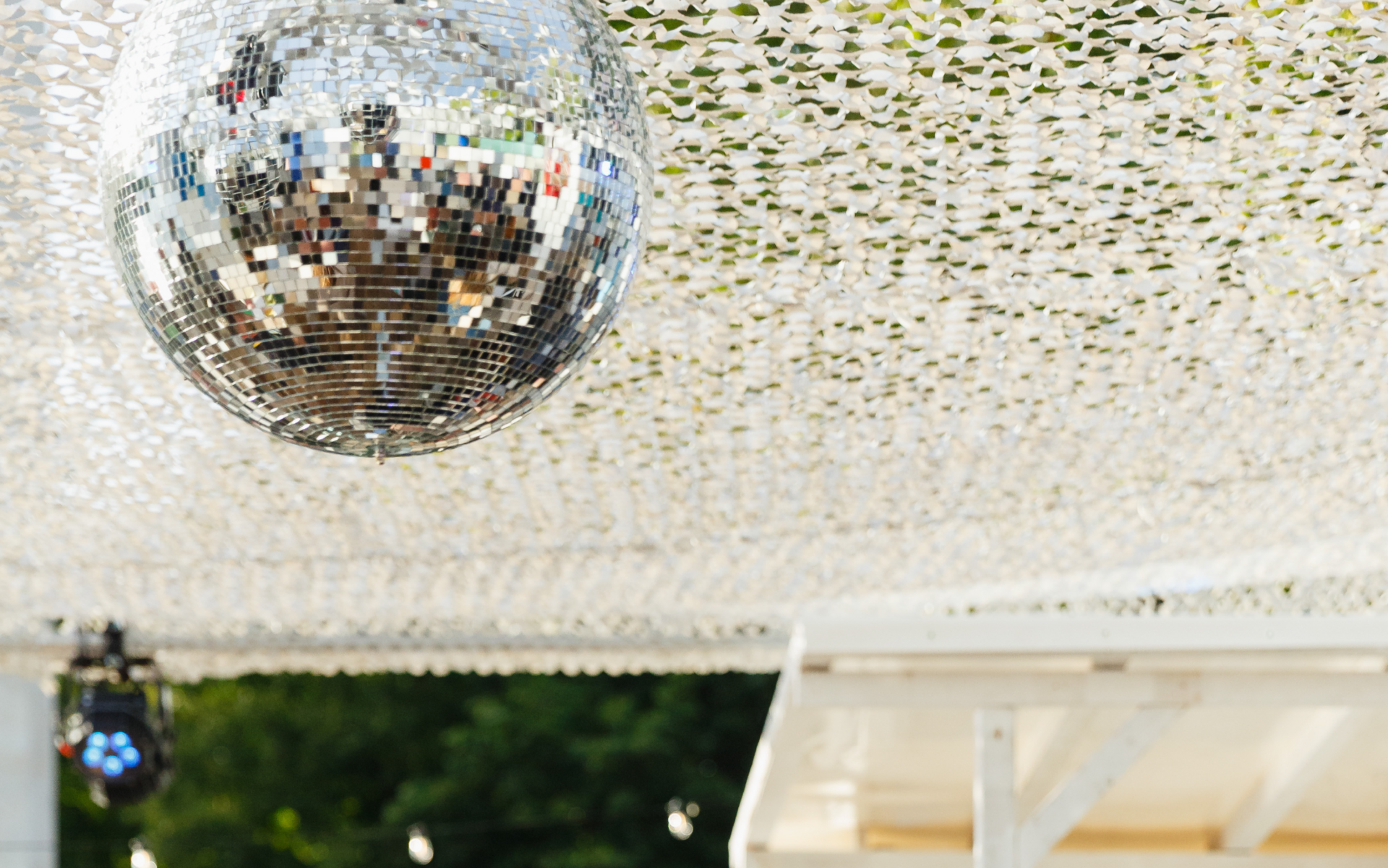 Man sieht eine Diskokugel, die draußen unter einem Weißen Netz hängt.